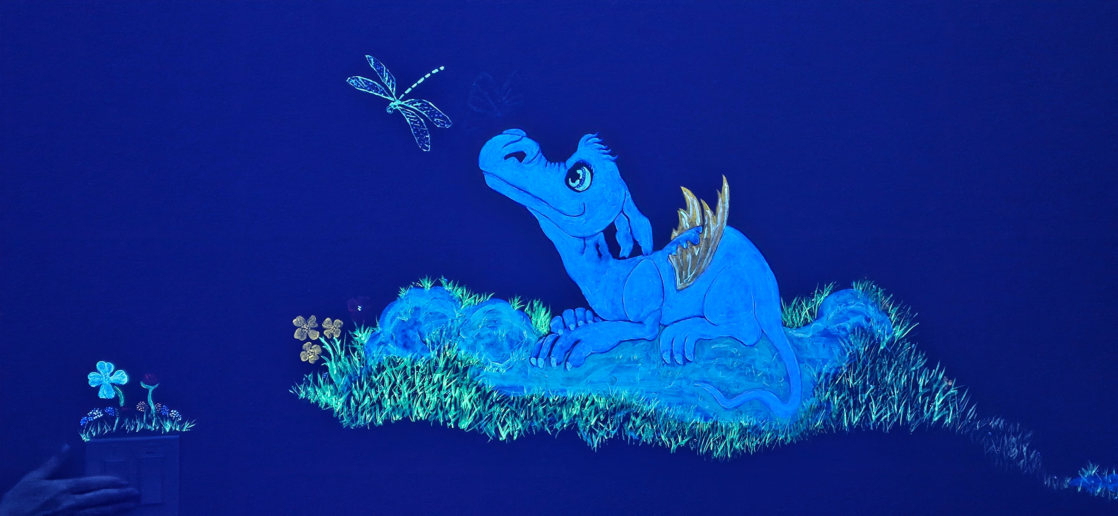 Glowing blue baby dragon watching a dragonfly in a meadow under black light in the Fantasy Room
