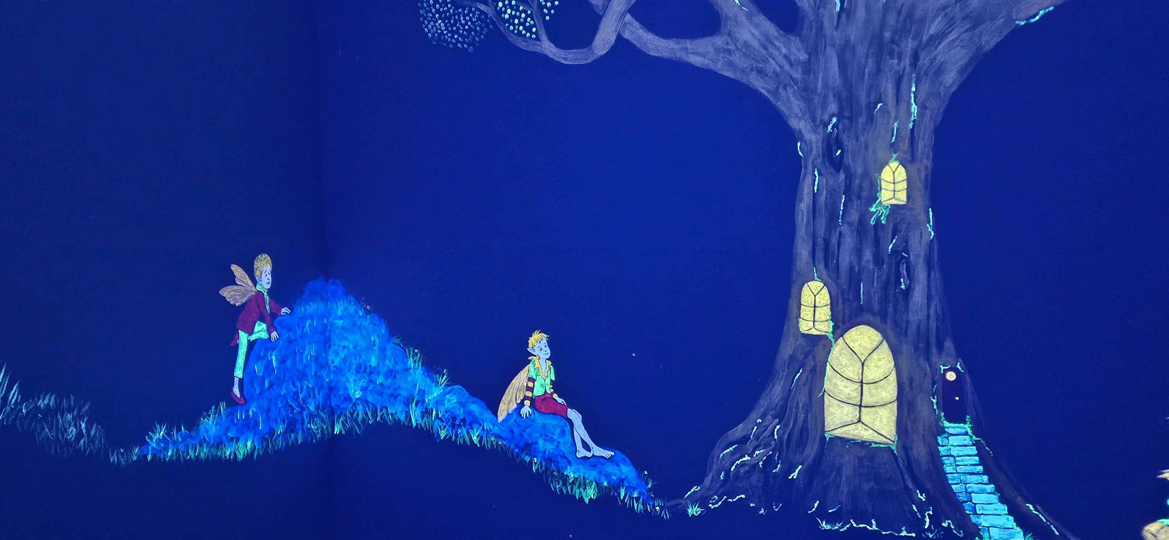 Glowing fairy children sitting on a hillside beside an enchanted tree with glowing windows under black light