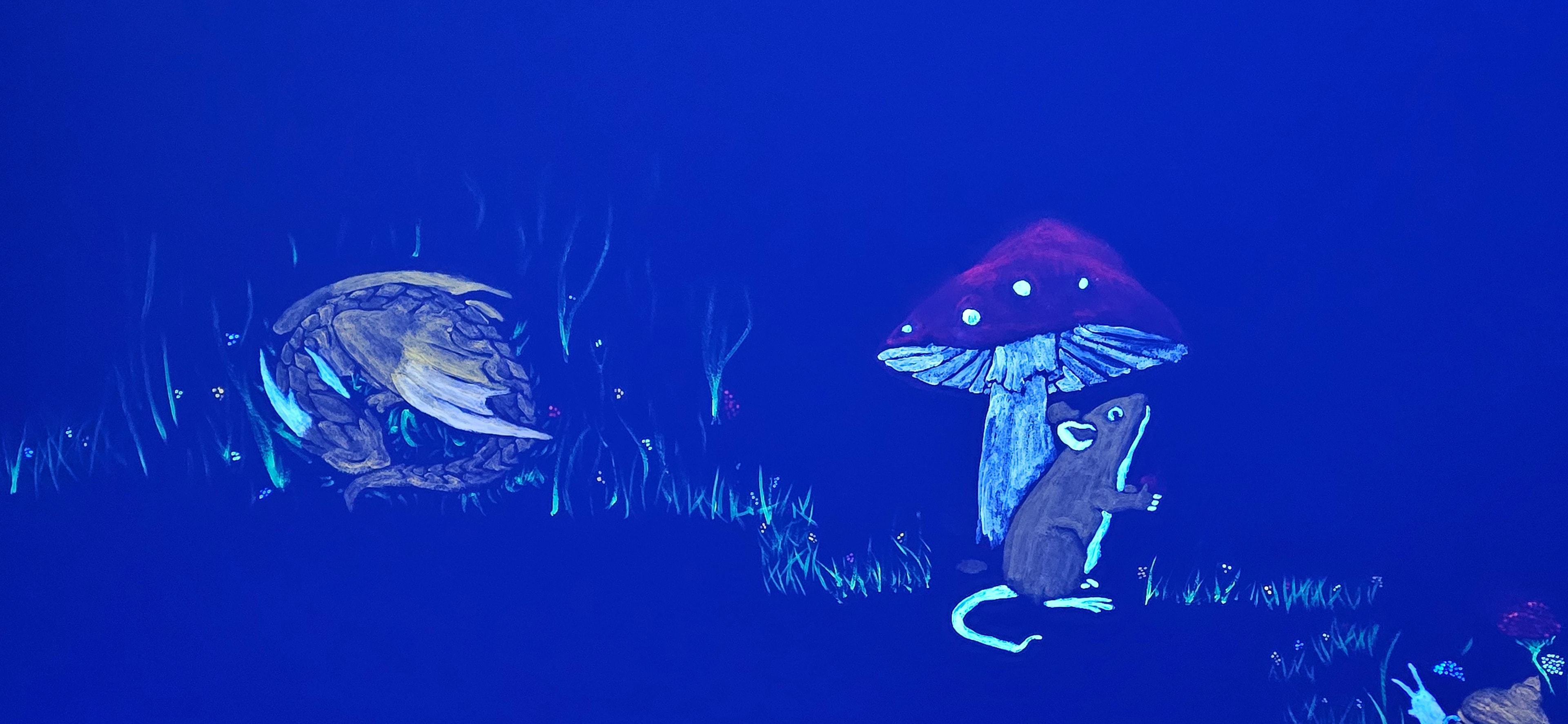 Glowing hedgehog and mouse sheltering under a red mushroom under black light in the Fantasy Room