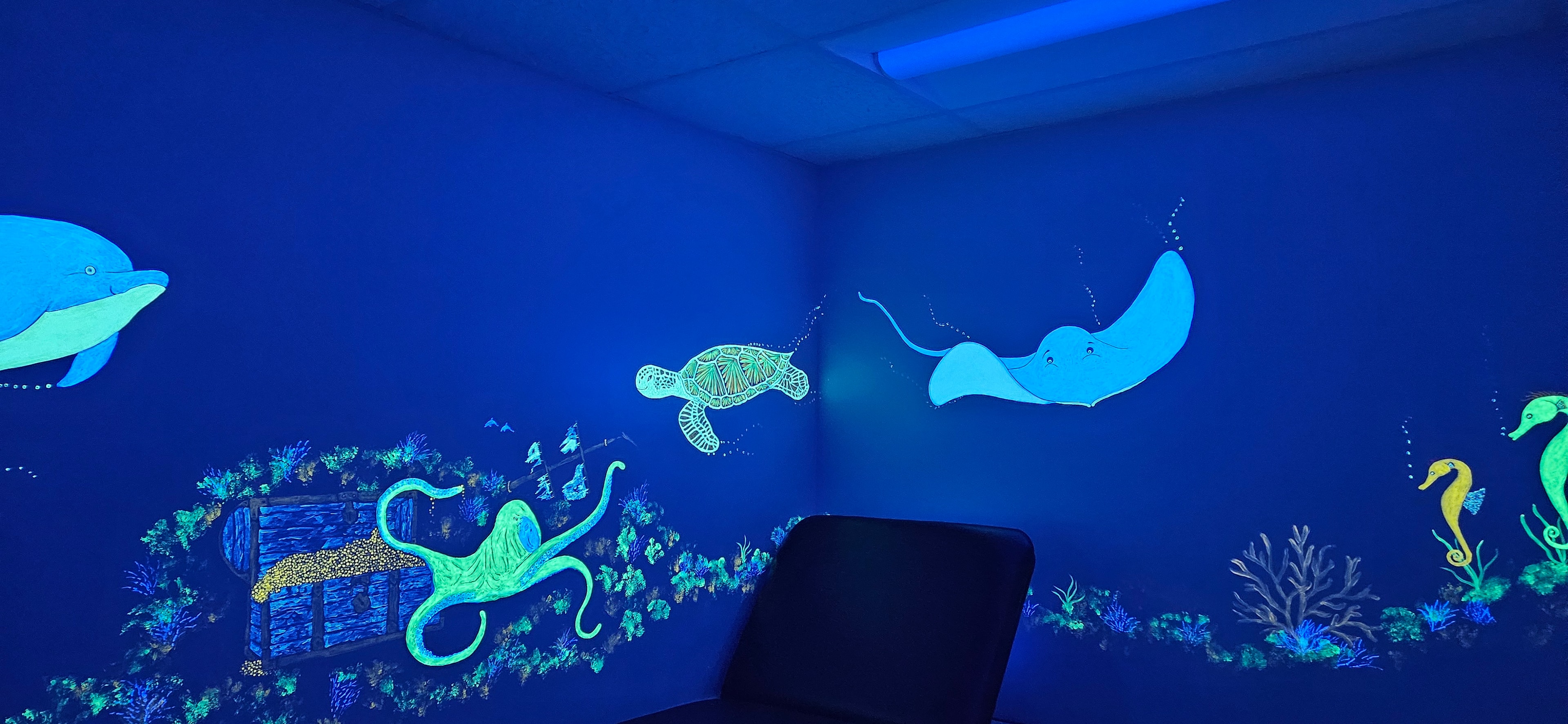 Ocean room glowing with dolphins, turtles, seahorses and coral under black light
