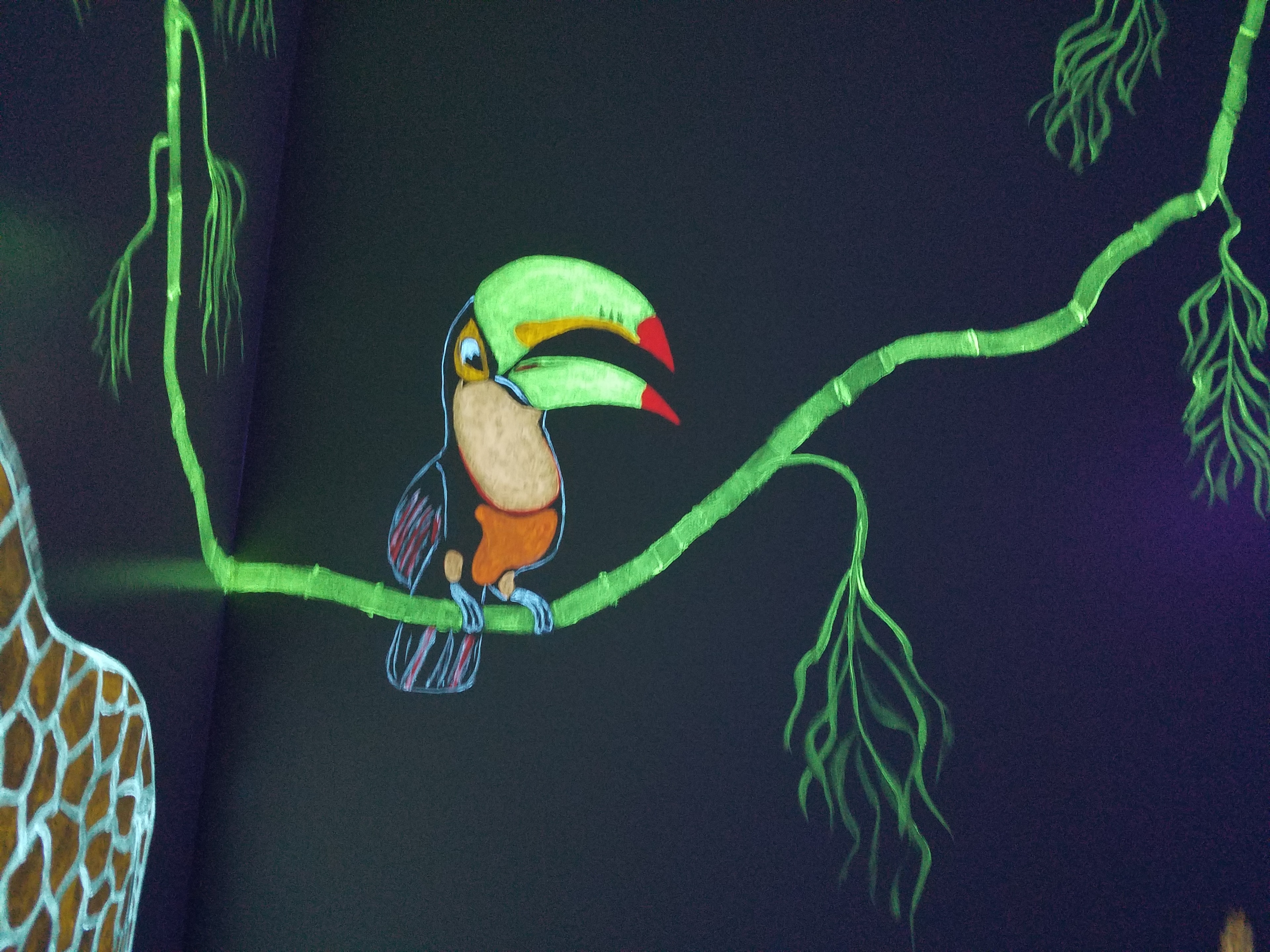 Glowing toucan perched on a bamboo branch in the Jungle Room under black light